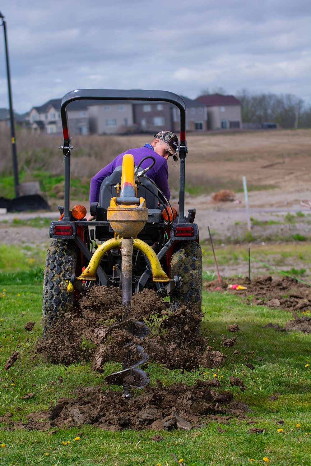 Concrete being poured around wooden fence post hole with yellow shovel and measuring equipment visible in Pickering yard