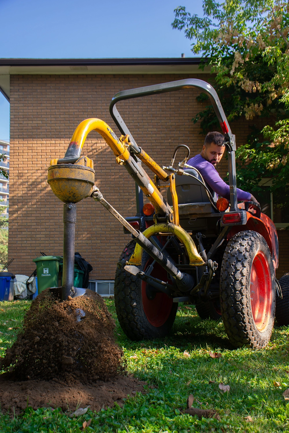 Bednarz hydraulic post hole auger mounted on compact tractor digging foundation for fence post at Port Dover backyard project