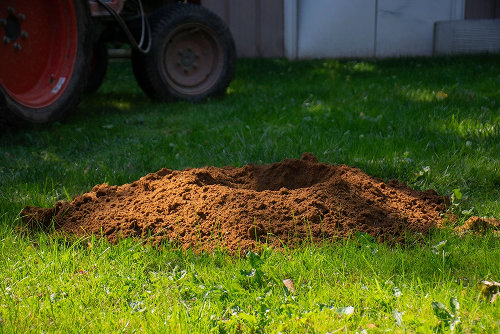 Freshly dug post hole with excavated clay soil mounded in a residential lawn — professional post hole digging service in Halton Hills Ontario
