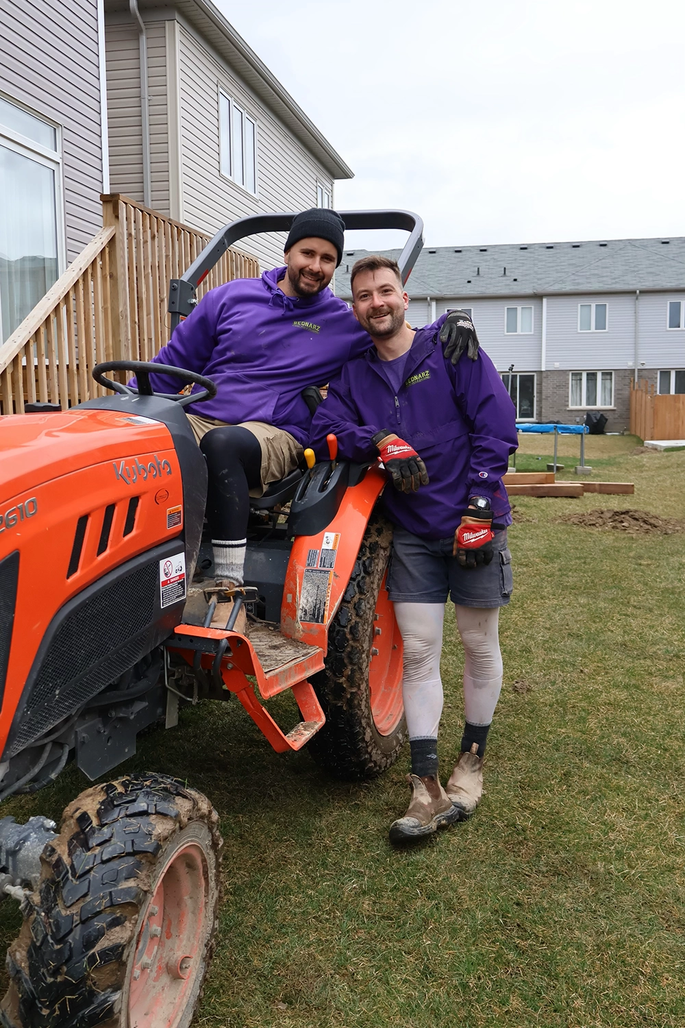 Bednarz crew member in purple shirt holding level tool at newly installed wooden deck footing post in residential Fergus yard