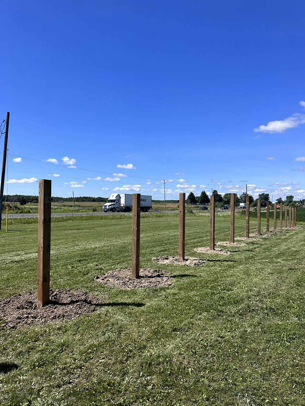 Long row of installed wooden fence posts set in excavated holes across open residential property in Fergus Ontario