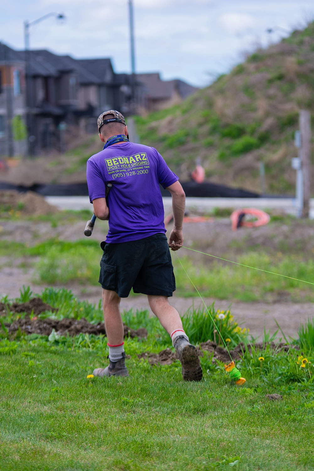 Bednarz crew member in purple shirt carrying string line for fence post alignment at Markham residential site