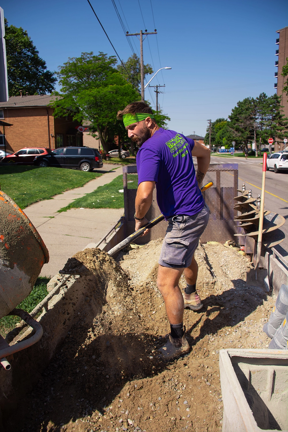Bednarz crew member in branded purple shirt manually digging post hole with shovel for fence installation in Norfolk County
