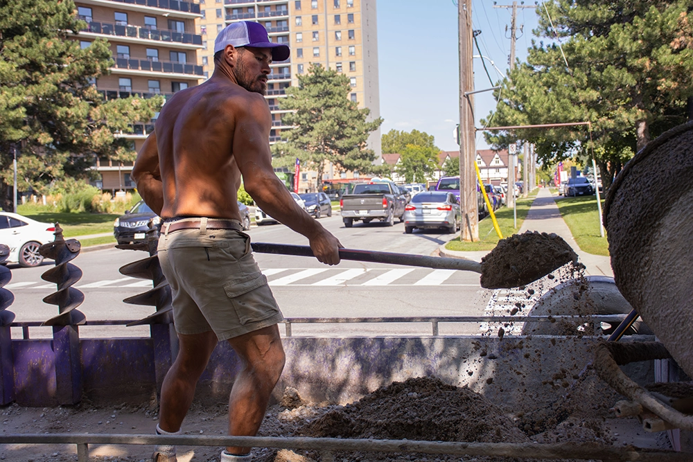 Bednarz crew member shoveling excavated soil on a post hole digging job in Ontario — post hole auger and equipment visible
