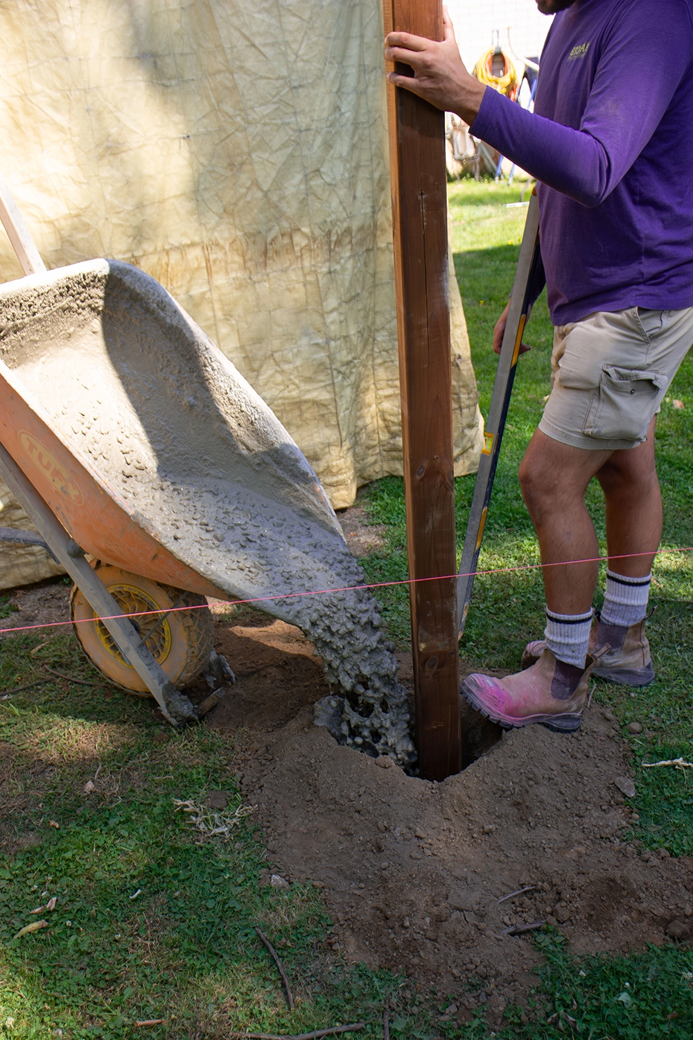 Bednarz technician pouring concrete around wooden fence post hole for secure installation in North York residential property