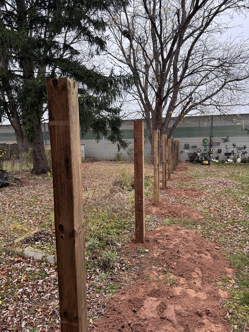 Wooden fence posts set in ground along established trees for residential fence in Mississauga Ontario