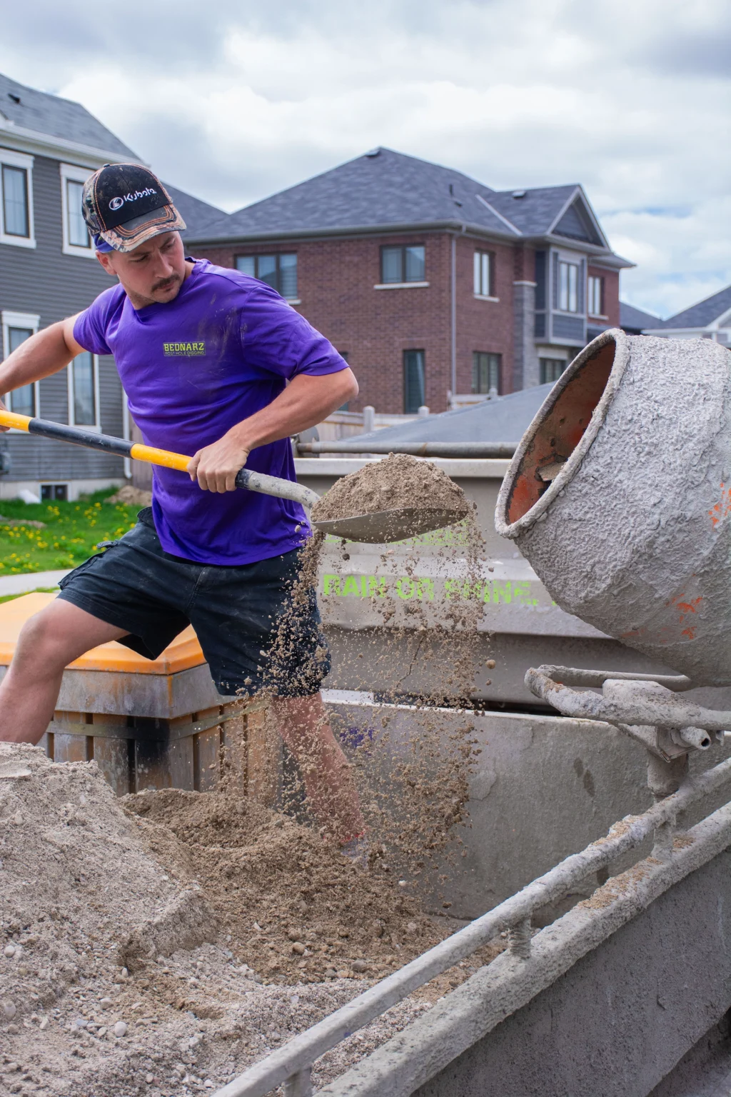 Bednarz crew member filling wheelbarrow with excavated soil from post hole for residential fence digging in Oakville Ontario