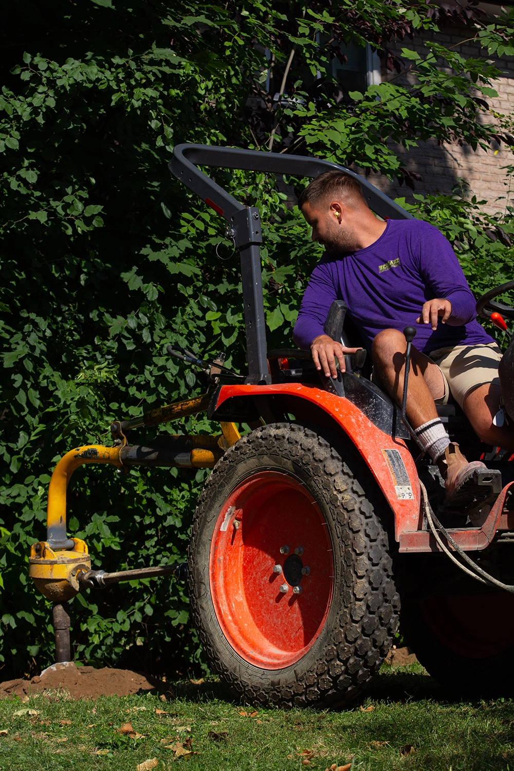 Bednarz operator sitting on compact hydraulic auger with orange wheel for fence post digging at Oakville backyard installation