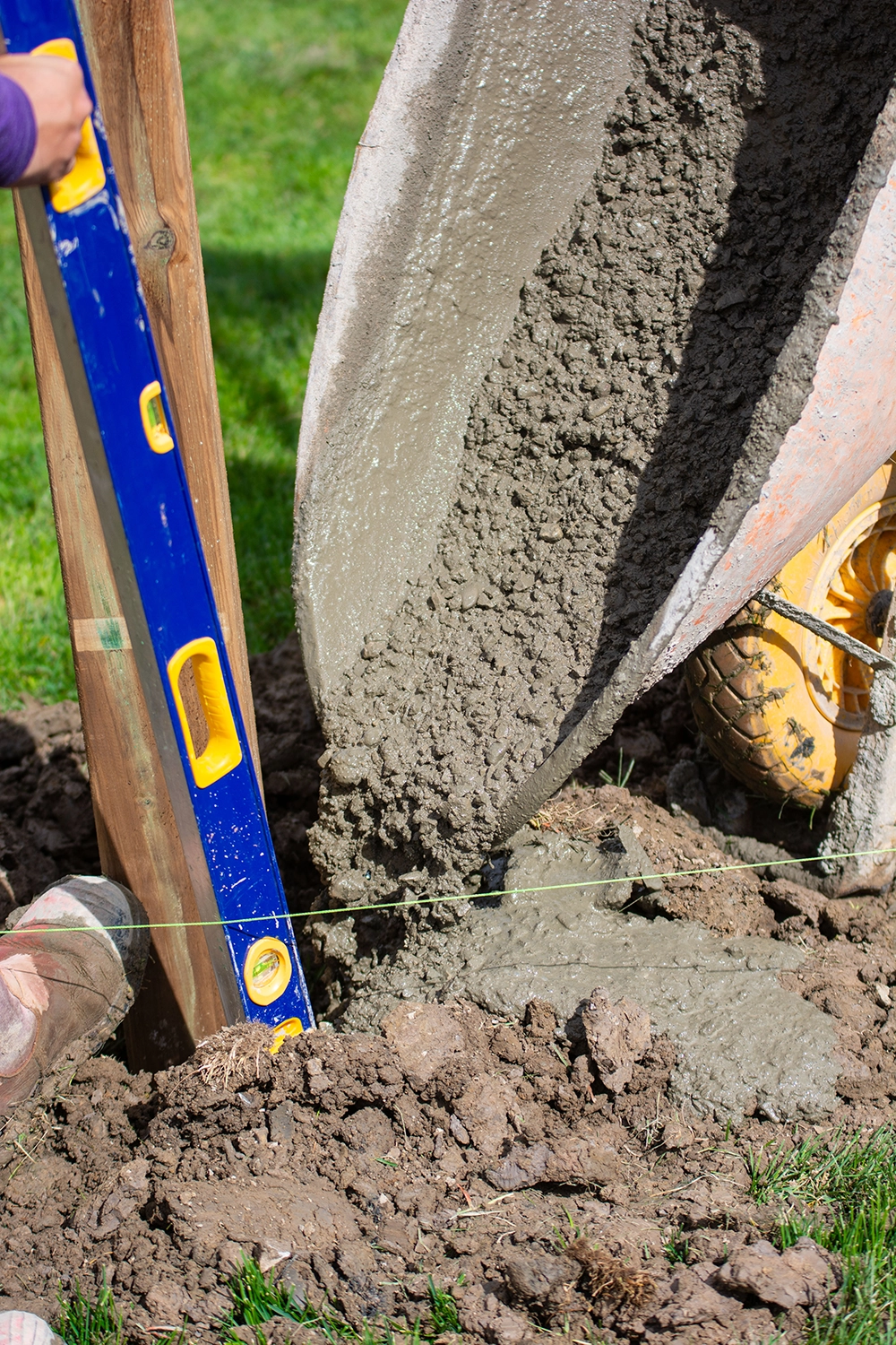 Close-up of concrete being poured into post hole with blue level tool against wooden fence post in Oakville residential yard