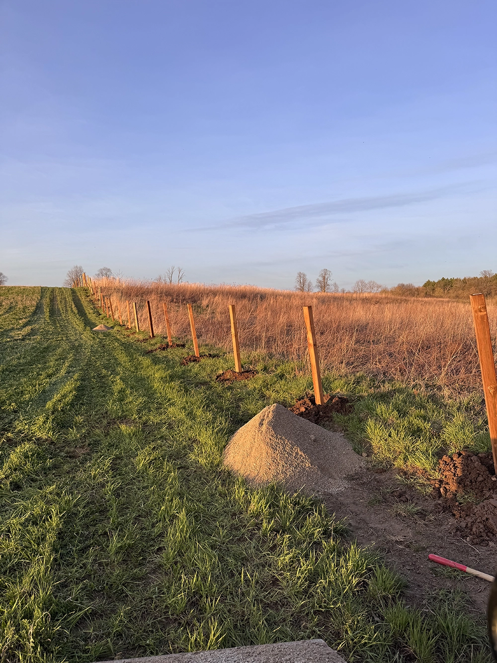Bednarz post hole drilling equipment setting fence posts in Tillsonburg agricultural field installation